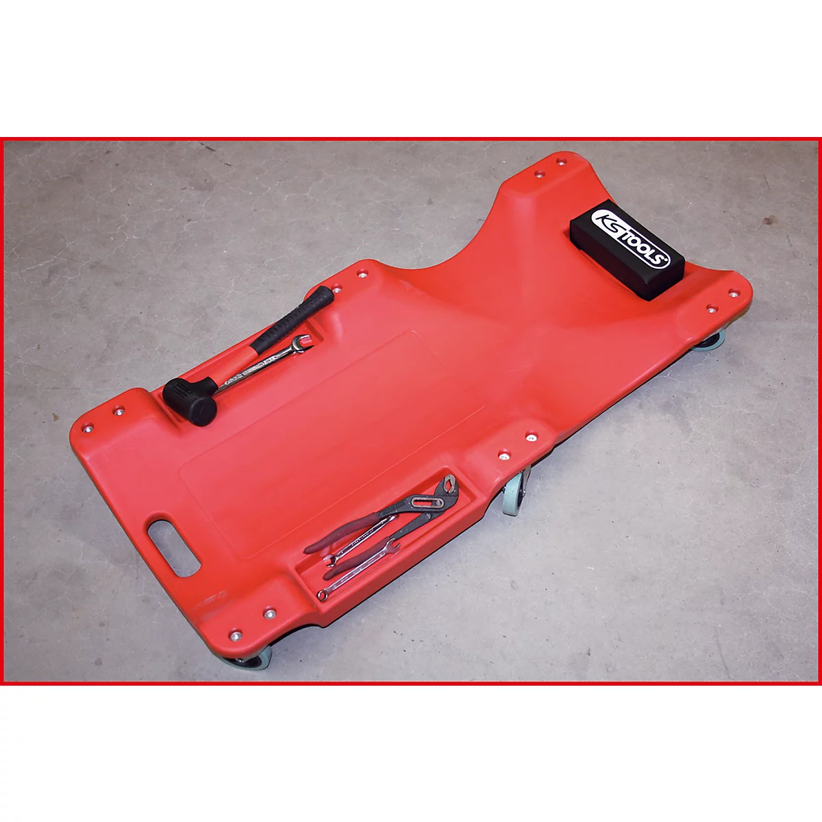 Rote Werkstattliege mit Werkzeug. Ein schwarzer Gummihammer, Schraubenschlüssel, Zangen und Schraubenschlüssel liegen auf der Liege.